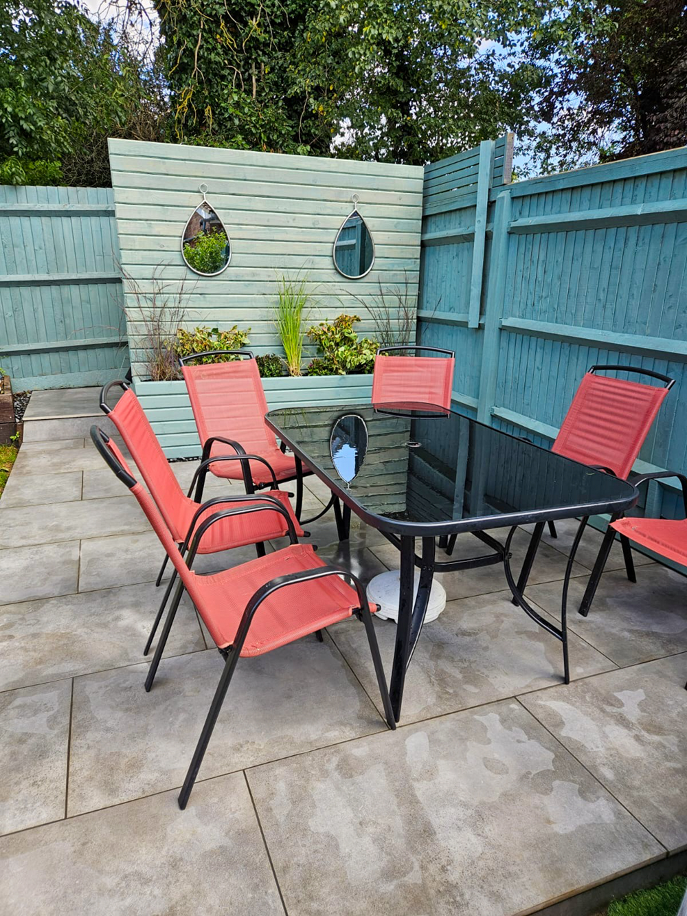 Grey porcelain patio with blue-green painted decorative wooden fence and planters
