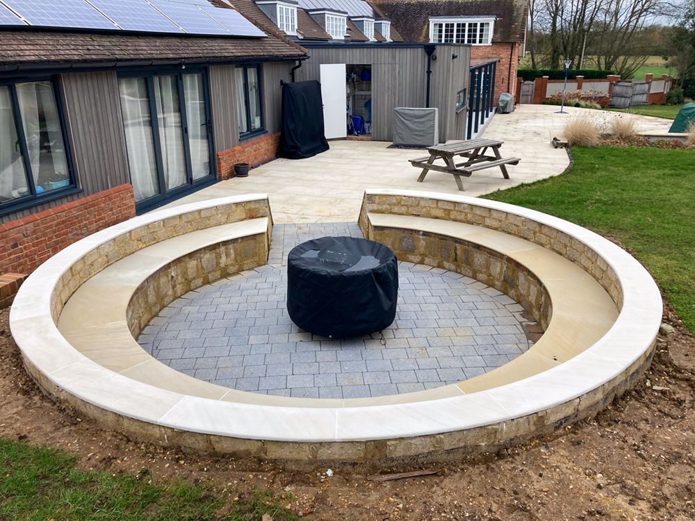 Circular sunken fire pit with grey block paving and curved stone walls with white coping