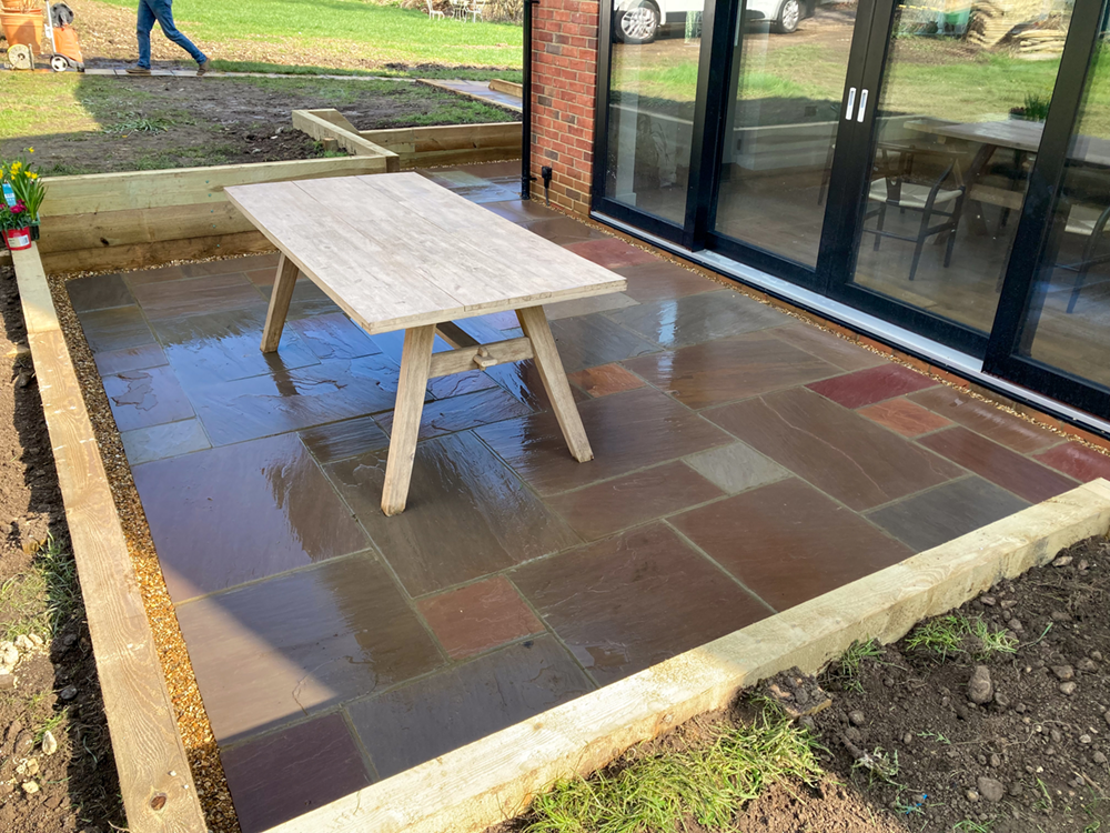 Multi-colored Indian sandstone patio with timber edging and gravel borders
