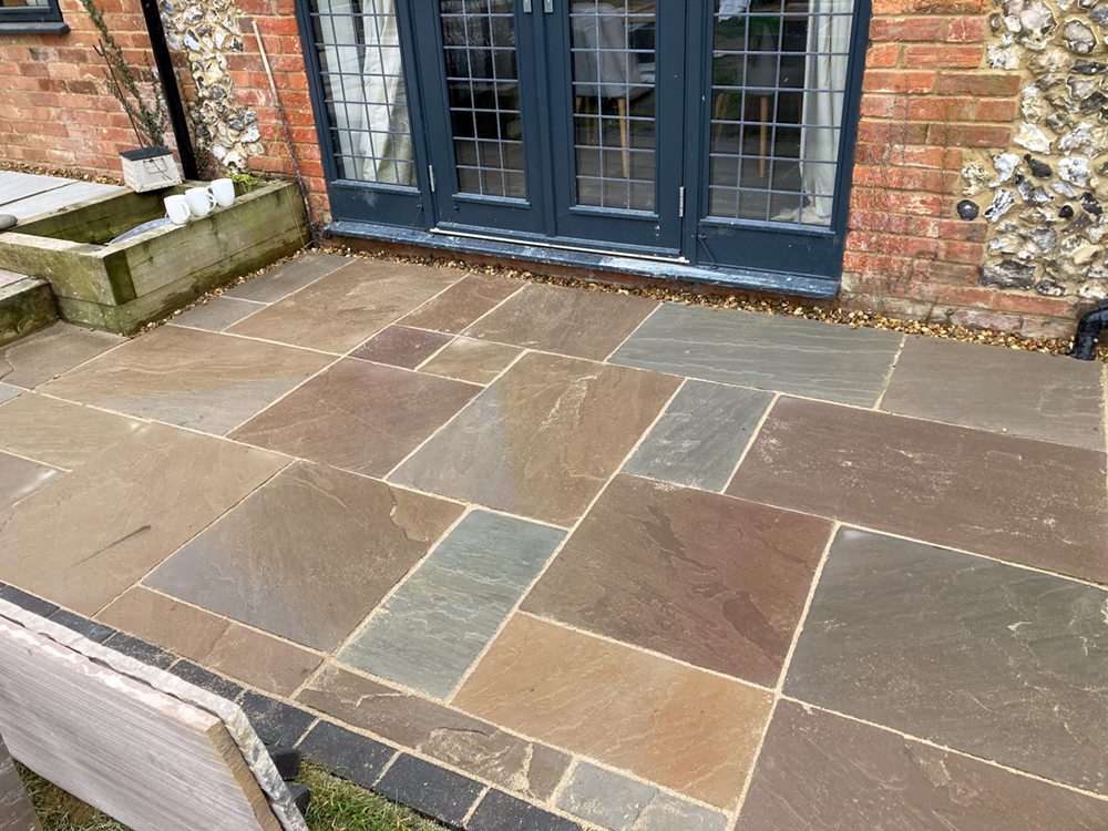 Random pattern Indian sandstone patio in brown tones near bi-fold doors