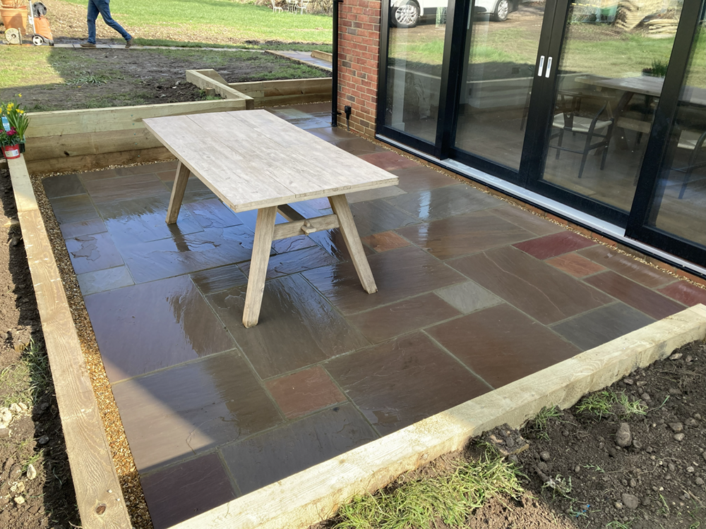 Raised multi-level Indian sandstone patio with timber sleeper borders in Reading